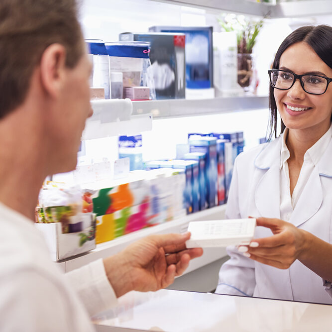 At the pharmacy. Beautiful young female pharmacist is offering a medication to a client while working at the cash desk